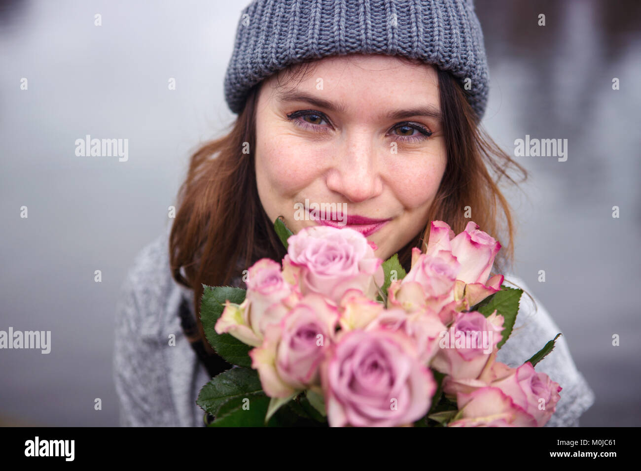 portrait of beautiful young woman outdoors with bouquet of pink roses ...