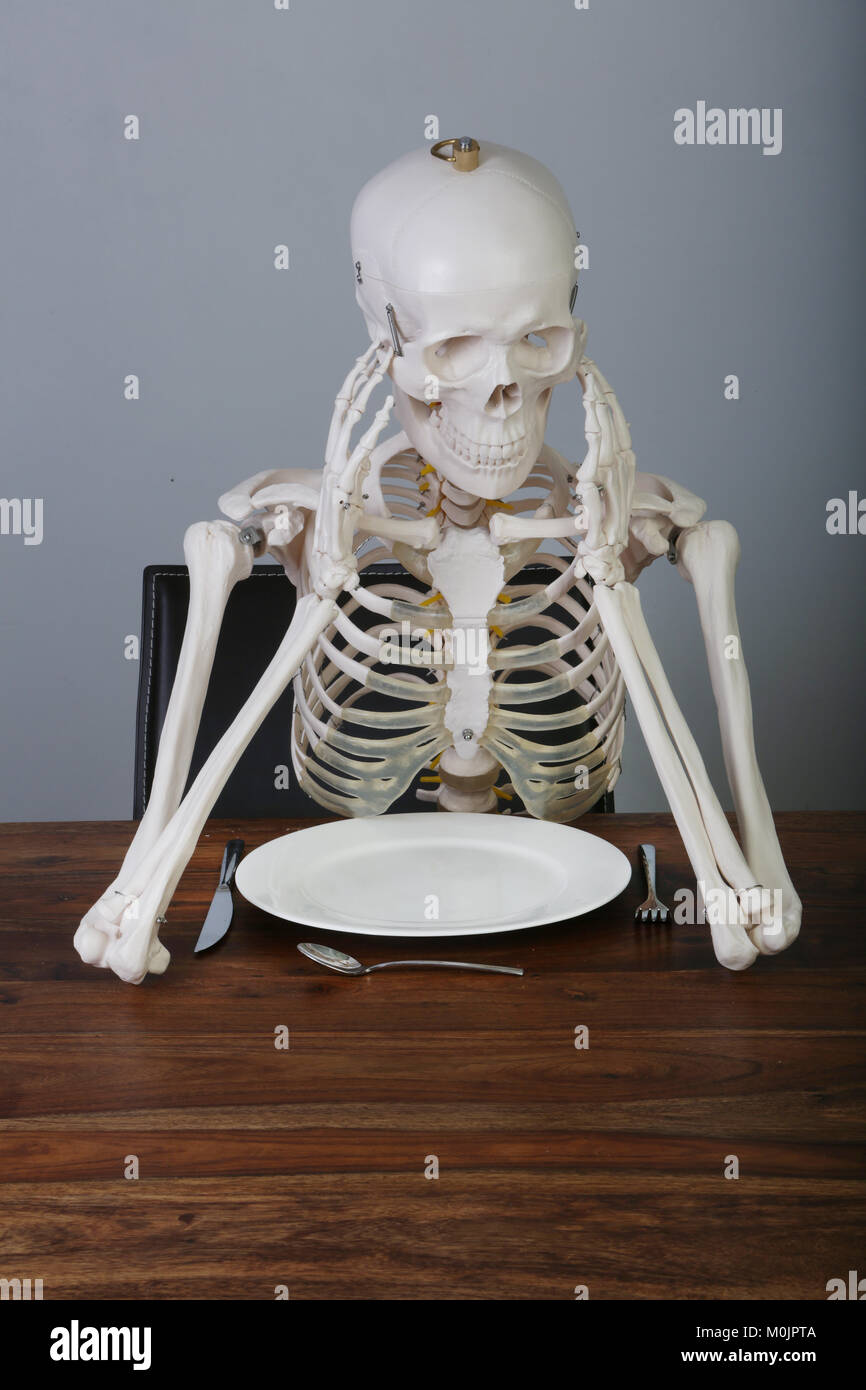 Skeleton with supported head sitting at table, Germany Stock Photo