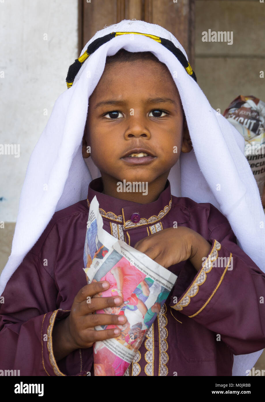 Young boy in traditional suit dressed for the Mawlid festival, eating popcorn, Lamu Island, Kenya Stock Photo