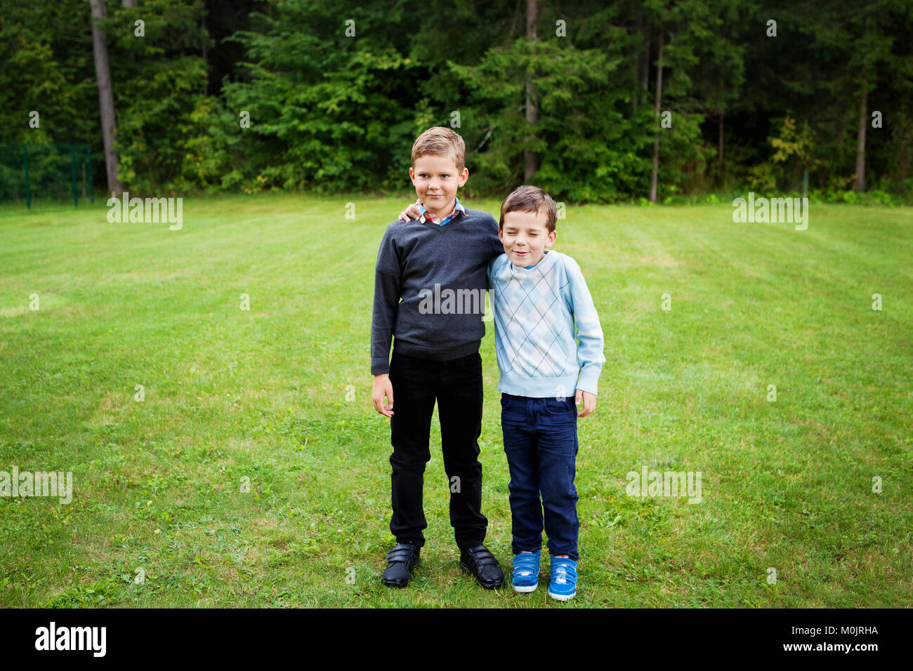 Two boys standing on lawn with hand on each shoulder dressed in formalwear -smiling, making fun, brothers portrait, togetherness, mischievous, bonding Stock Photo
