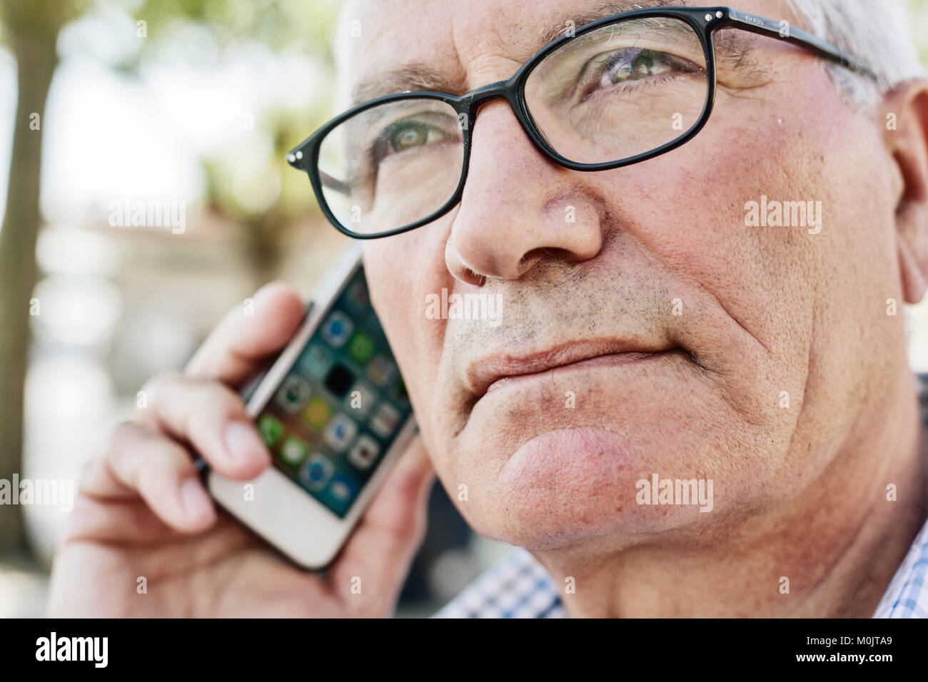 Grey-haired senior with glasses talking on the phone with his smartphone, Germany Stock Photo