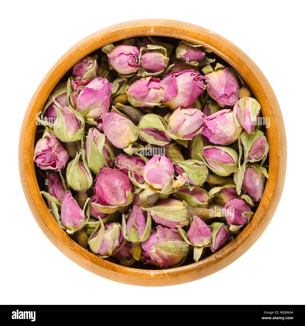 Dried rose buds in wooden bowl. Flowering plant of the genus Rosa. Used as decoration, as scent, for teas and perfums. Isolated macro food photo. Stock Photo