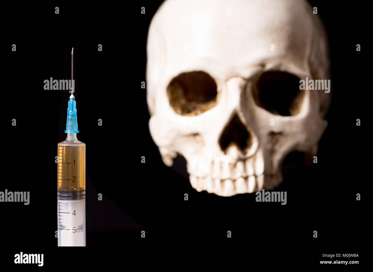Syringe with brown liquid and blurry skull isolated on black background Stock Photo