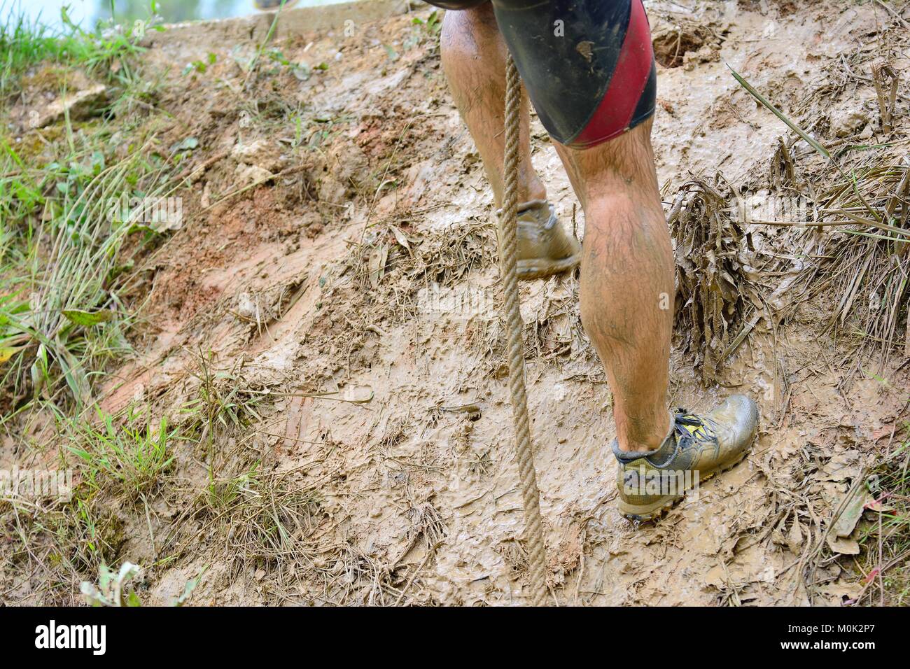 Unrecognizable man climbing slope with rope in mud Stock Photo - Alamy
