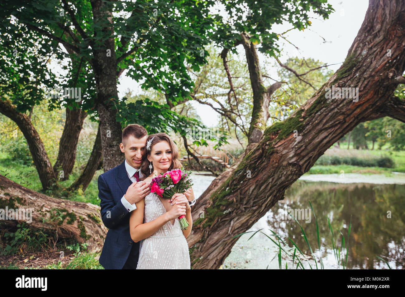 Groom bride with a bouquet hugging in park Stock Photo - Alamy