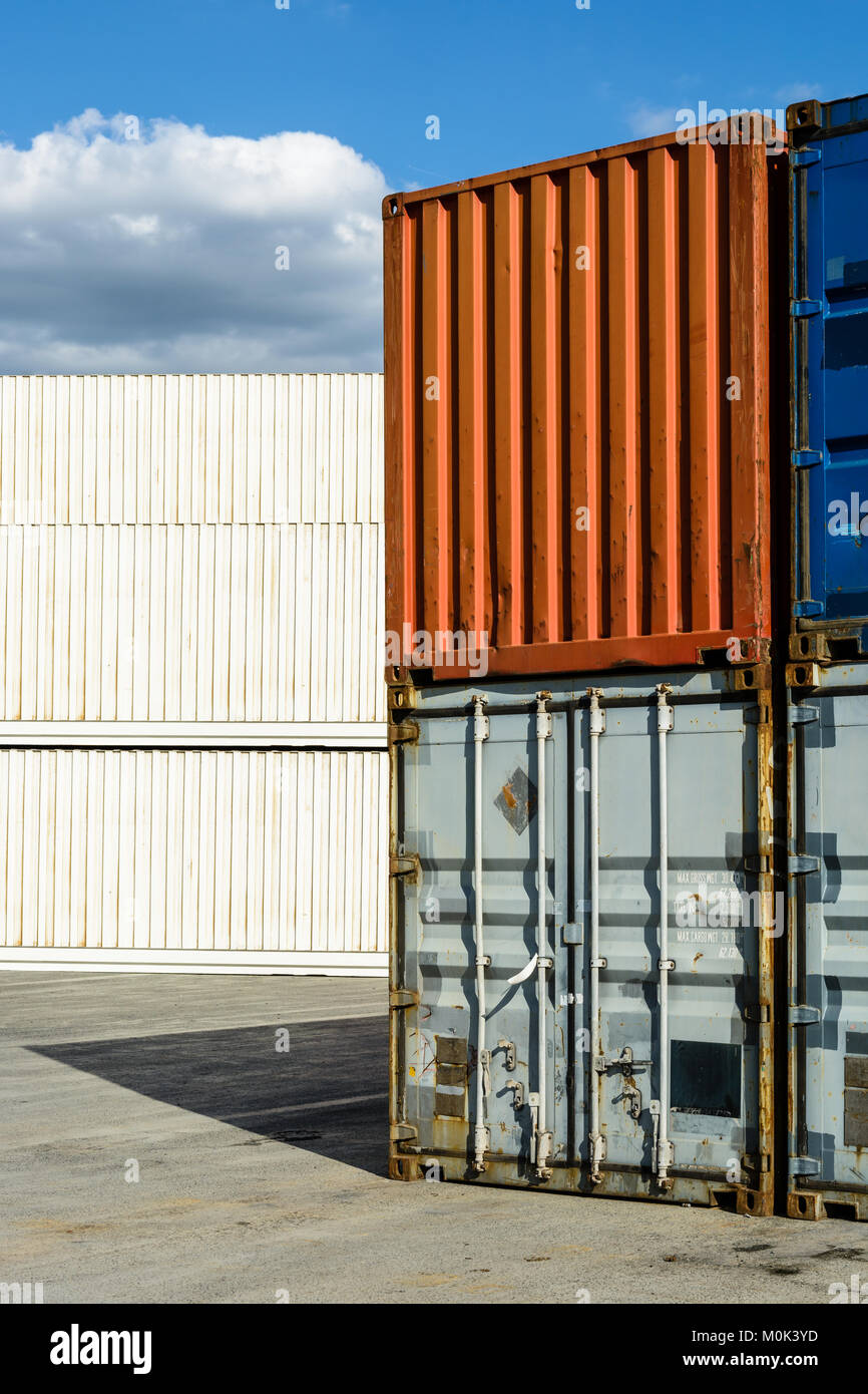 Worn intermodal containers stacked in a shipping yard with newer white pallet wide and refrigerated containers in the background. Stock Photo