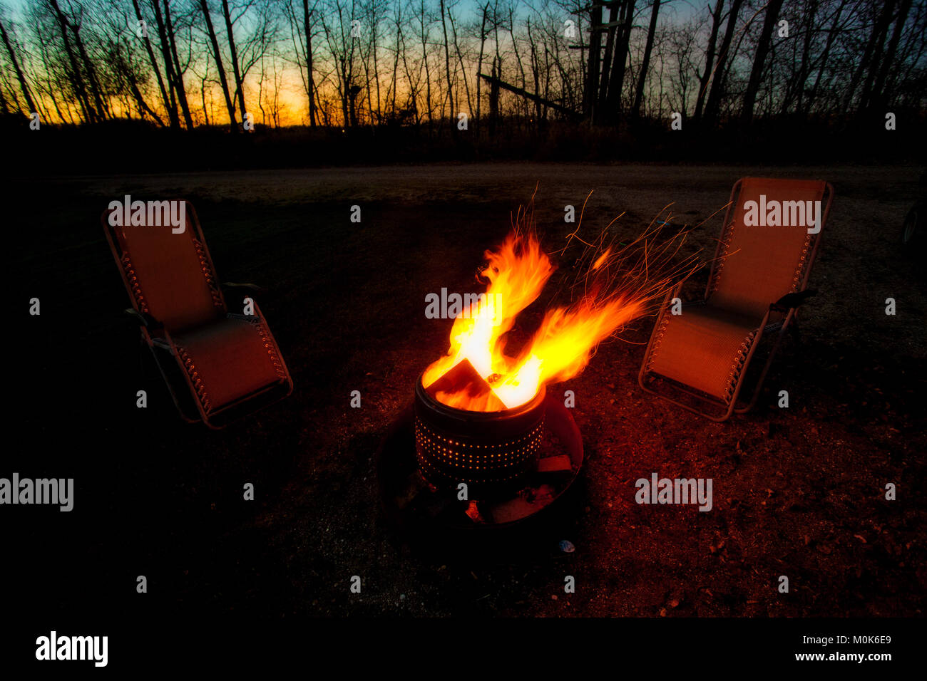 Two lounging chairs by a roaring campfire at dusk in a night time rural