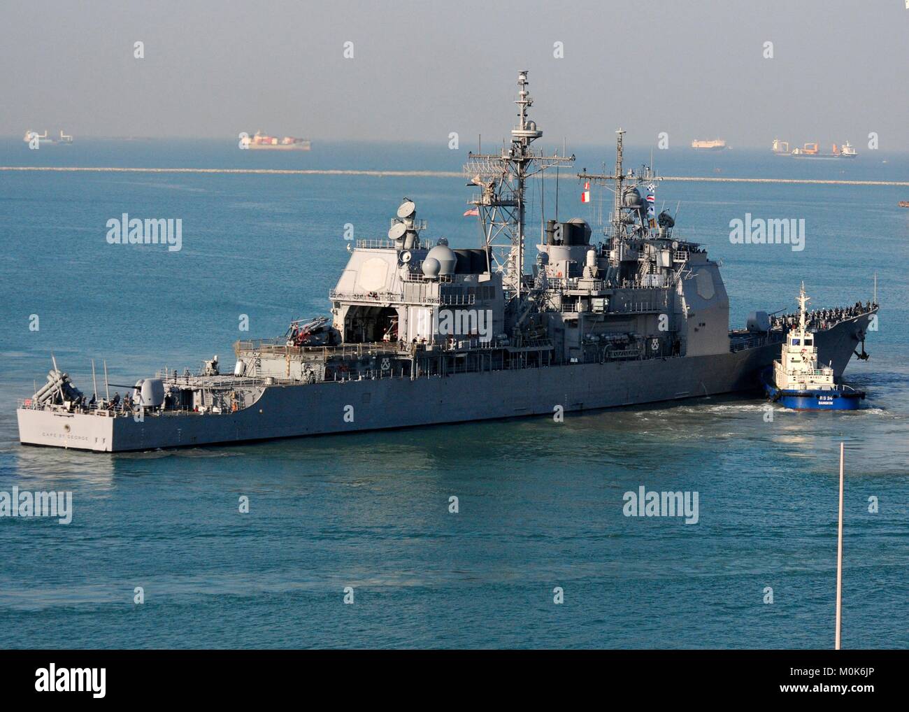 A tugboat guides the U.S. Navy Ticonderoga-class guided-missile cruiser USS Cape St. George out of port January 10, 2012 in Laem Chabang, Thailand. Stock Photo