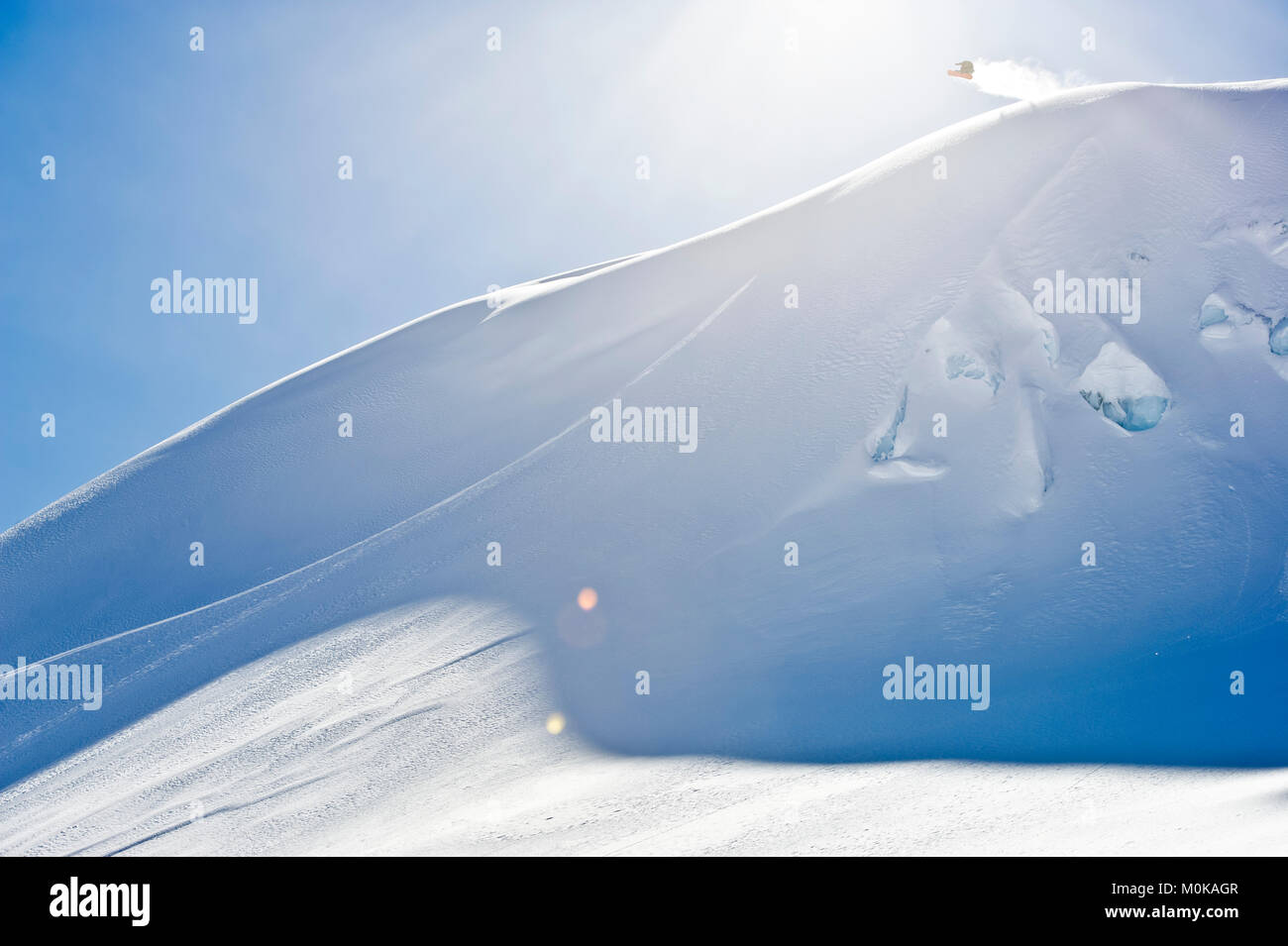A professional, freeriding snowboarder in mid-air on a snowy slope against a blue sky; British Columbia, Canada Stock Photo