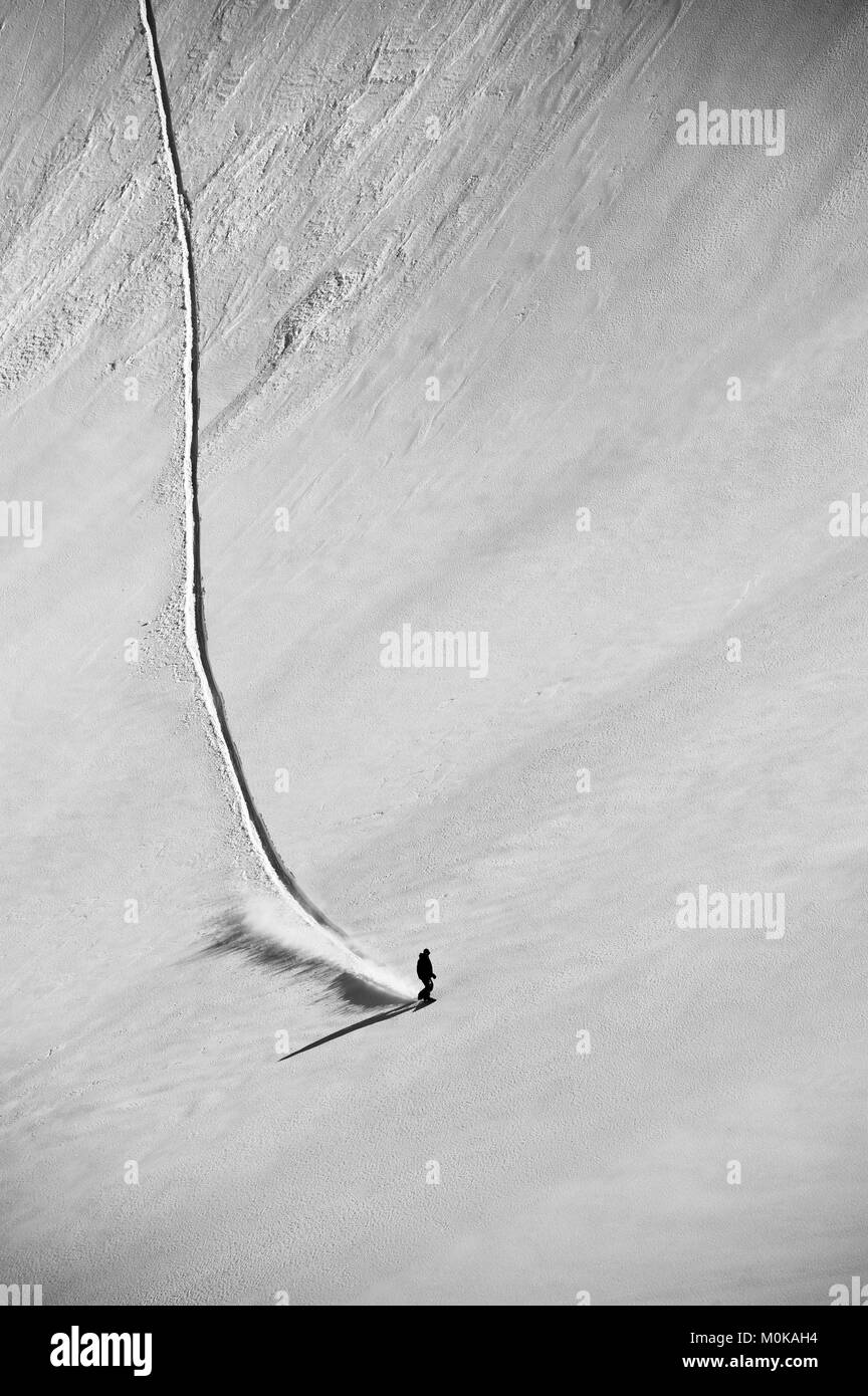 A professional, freeriding snowboarder on a wide open snowy slope making new tracks; British Columbia, Canada Stock Photo