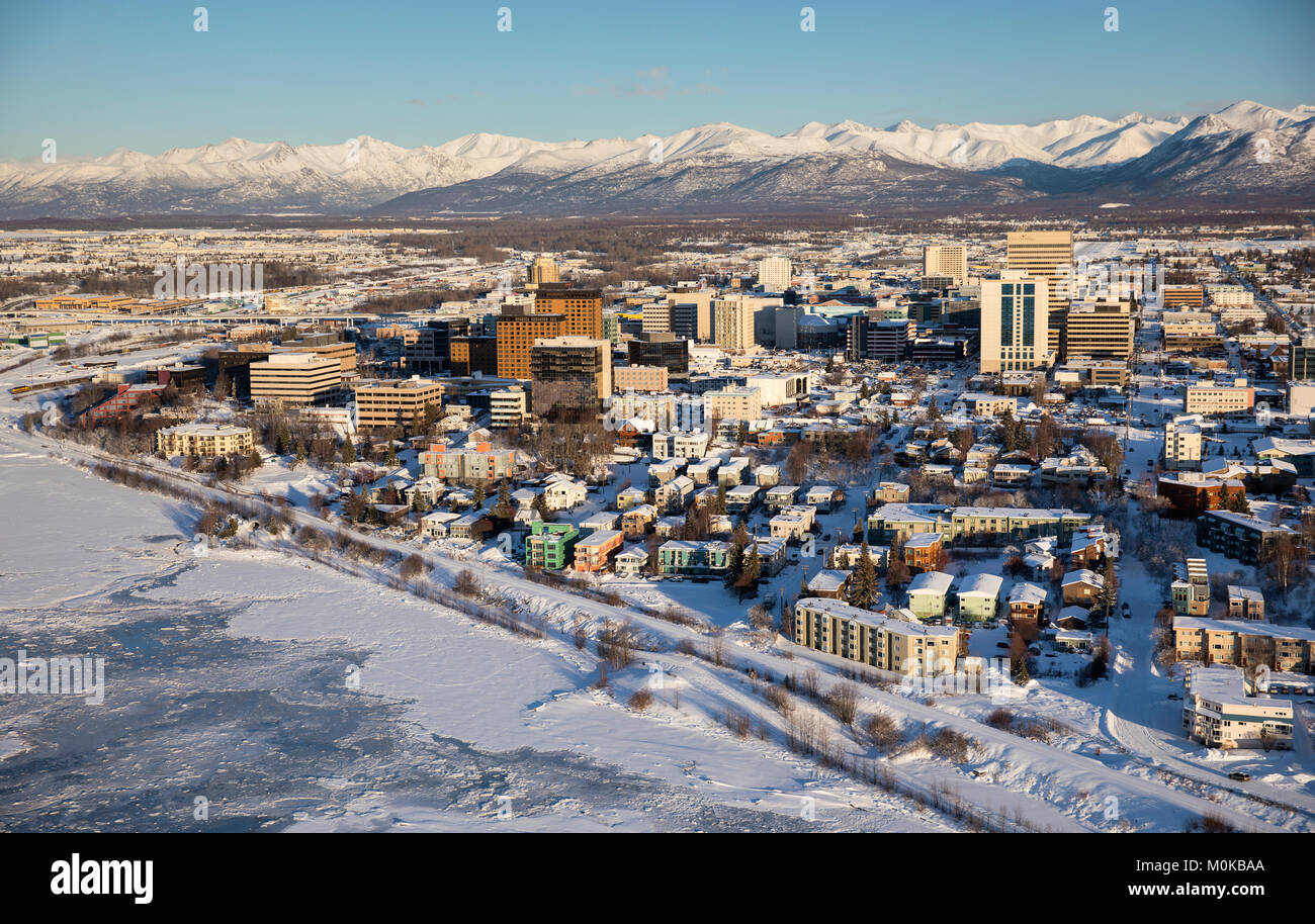 Aerial view of snow covering the sea ice on the frozen shores of downtown Anchorage, the Chugach Mountains in the distance beyond the office buildi... Stock Photo