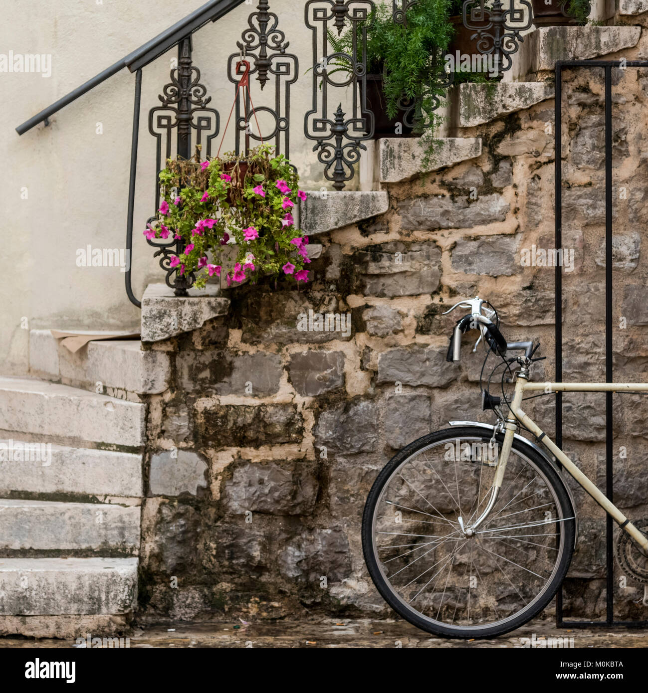 A bicycle parked beside a stone wall with steps leading up and plants decorating the railing; Budva, Opstina Budva, Montenegro Stock Photo