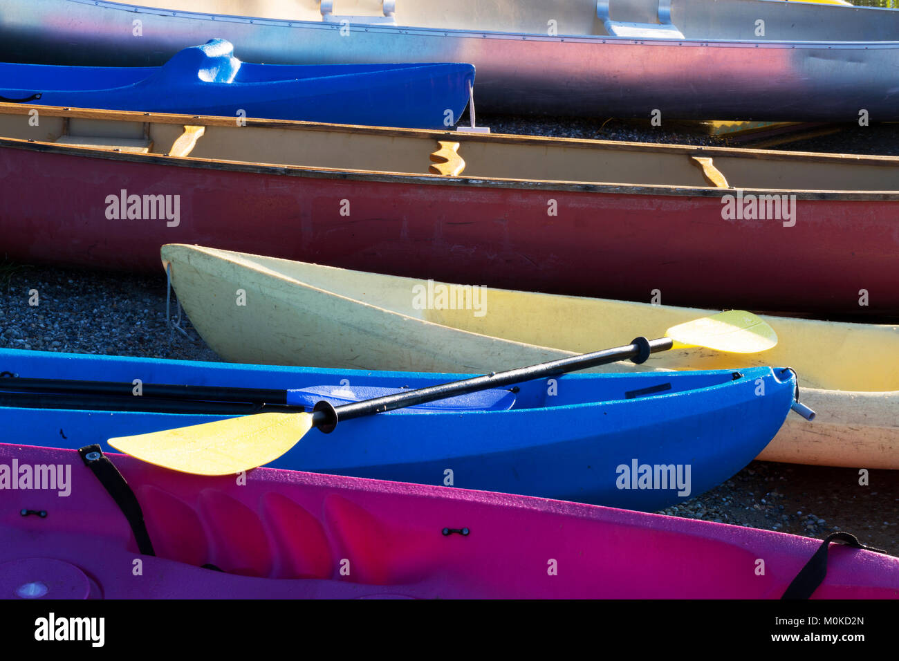 A variety of coloured canoes and kayaks on the shore with a paddle