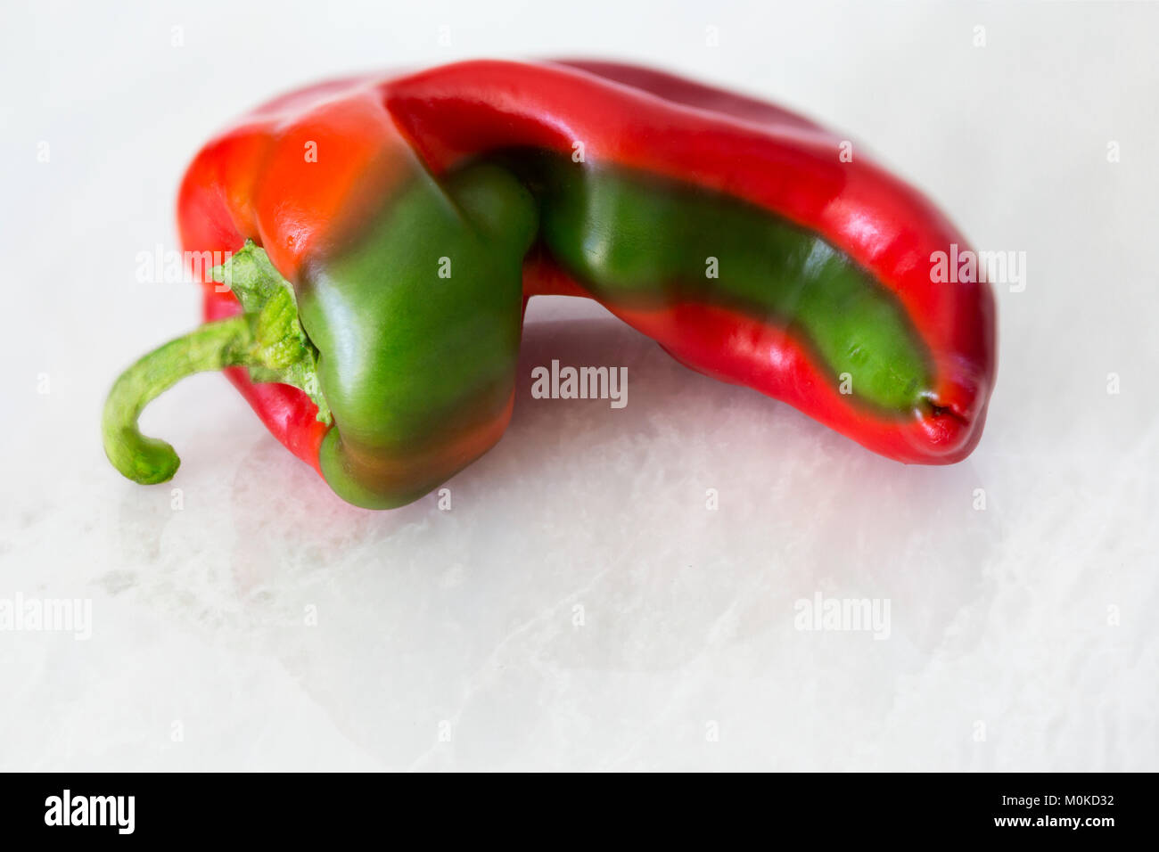 A red bell pepper in a unique shape and with a green stripe laying on a marble counter Stock Photo