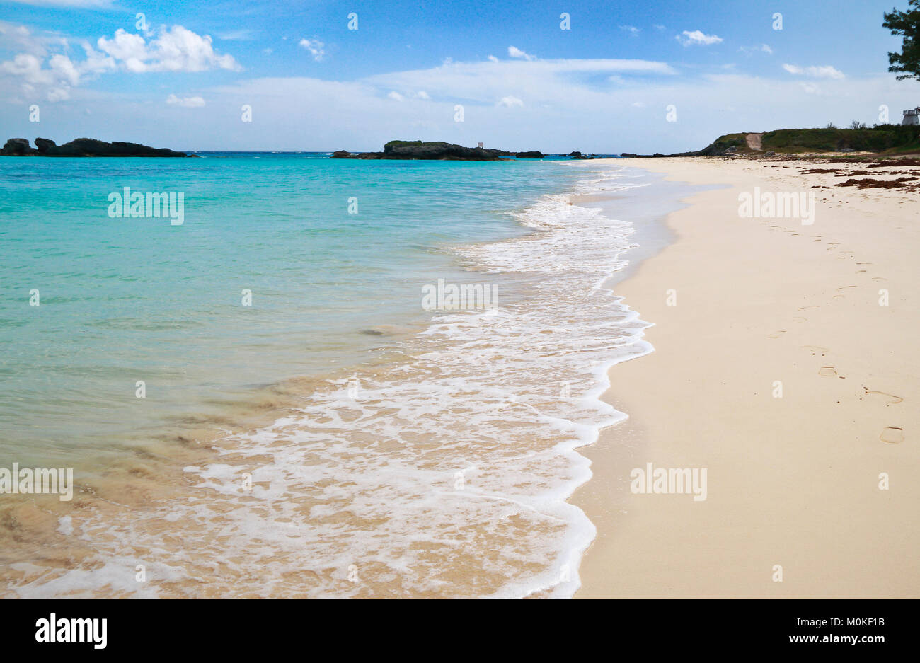 Bermuda beach with foot prints along turquoise sea water in Long Bay, Copper's Island Nature Reserve, under blue sky and white clouds Stock Photo
