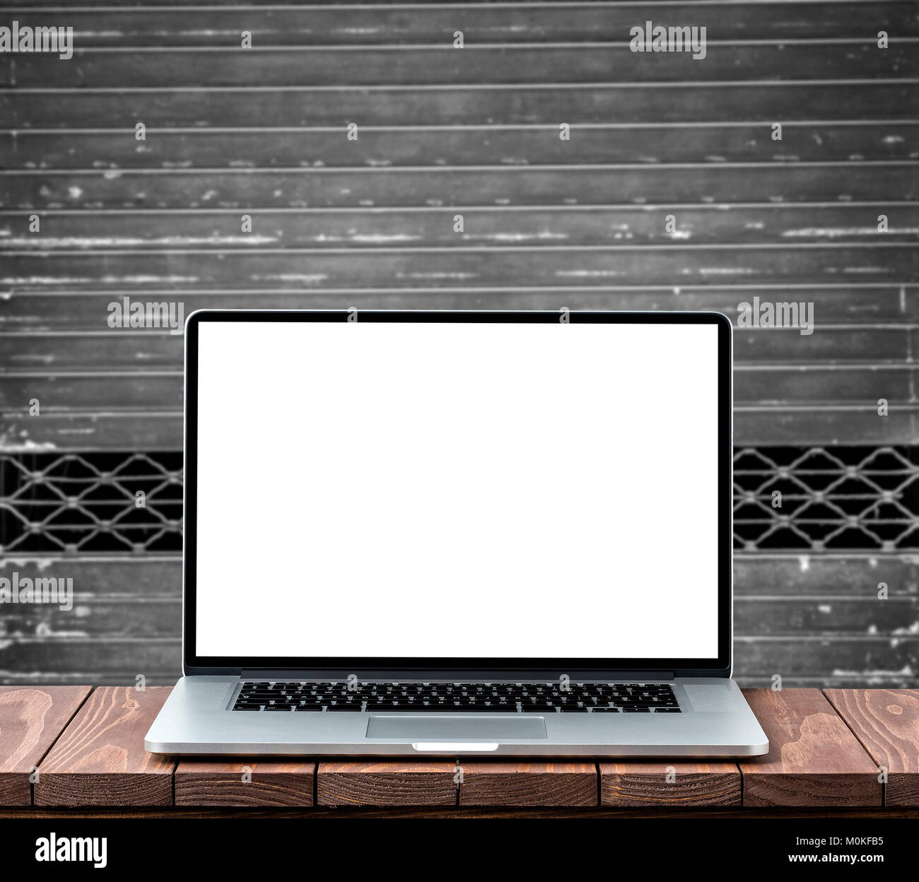 Modern laptop with empty white screen on wooden table against old metal ...