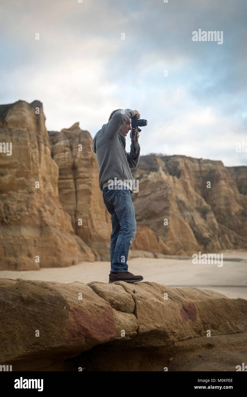 man standing on rocks by rugged coastline taking a photo. Stock Photo