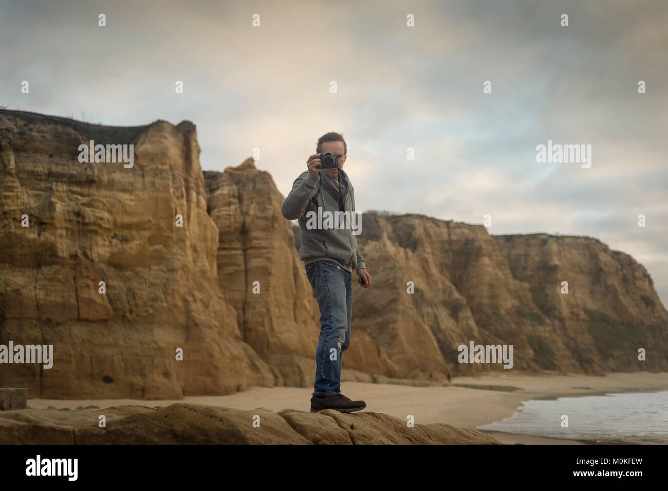 man standing on rocks by rugged coastline taking a photo. Stock Photo