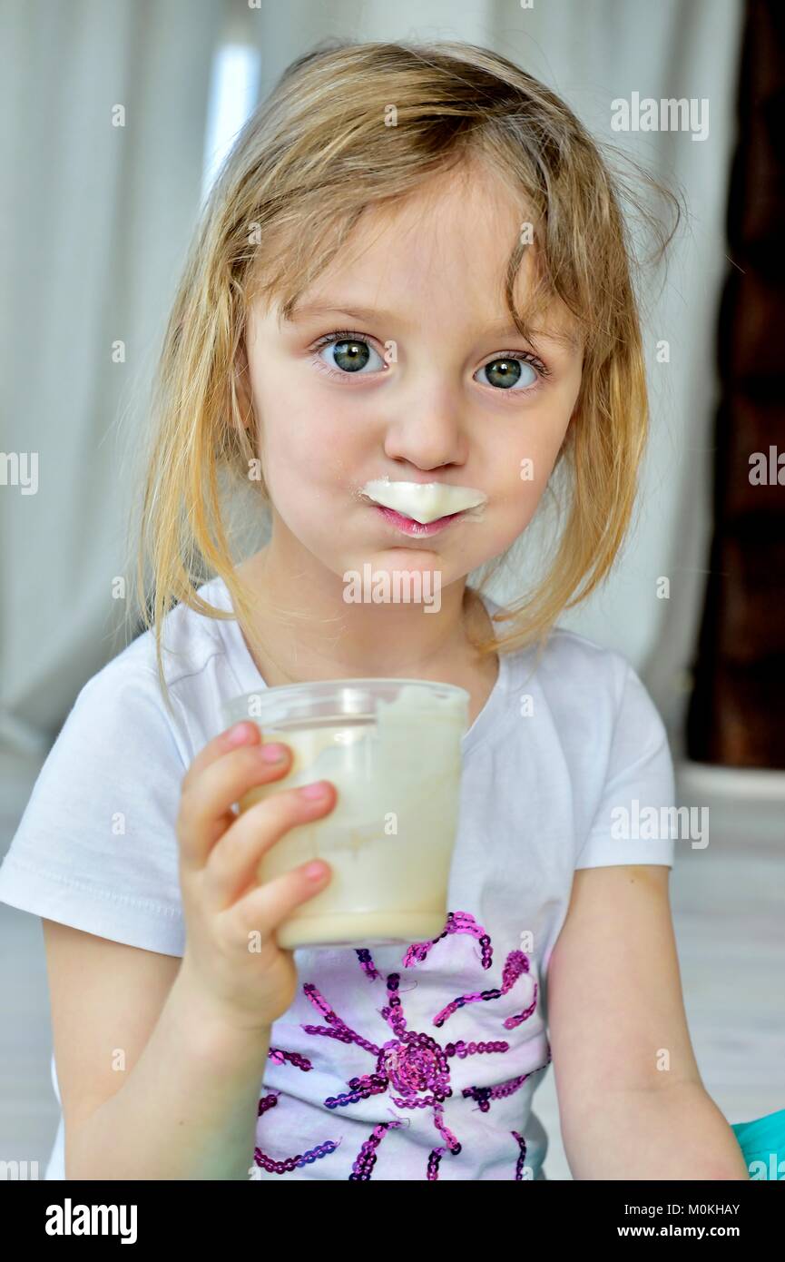 Close up fun portrait of cute  little girl with milk moustaches. Portrait of a little happy girl with yogurt on the face. Stock Photo