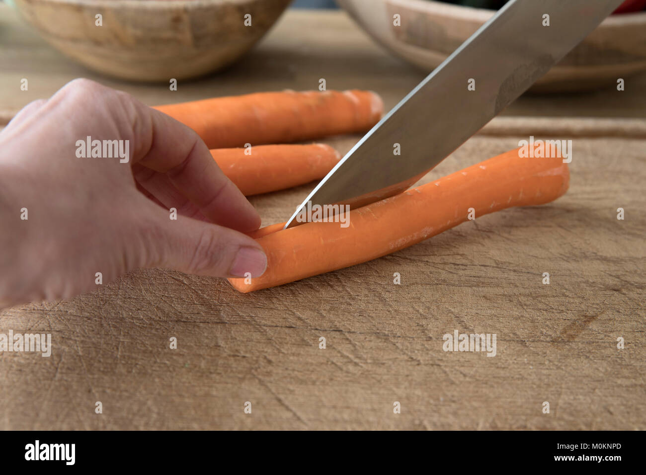 Knife skills cutting slicing carrot in half safely cutting away from fingers stabilizing food. Stock Photo