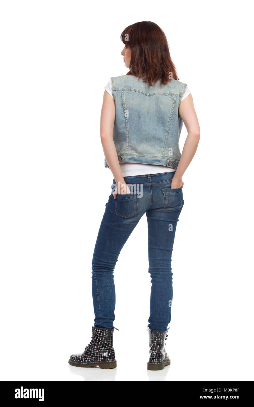 Young woman in jeans vest and black boots is standing, holding hands in ...