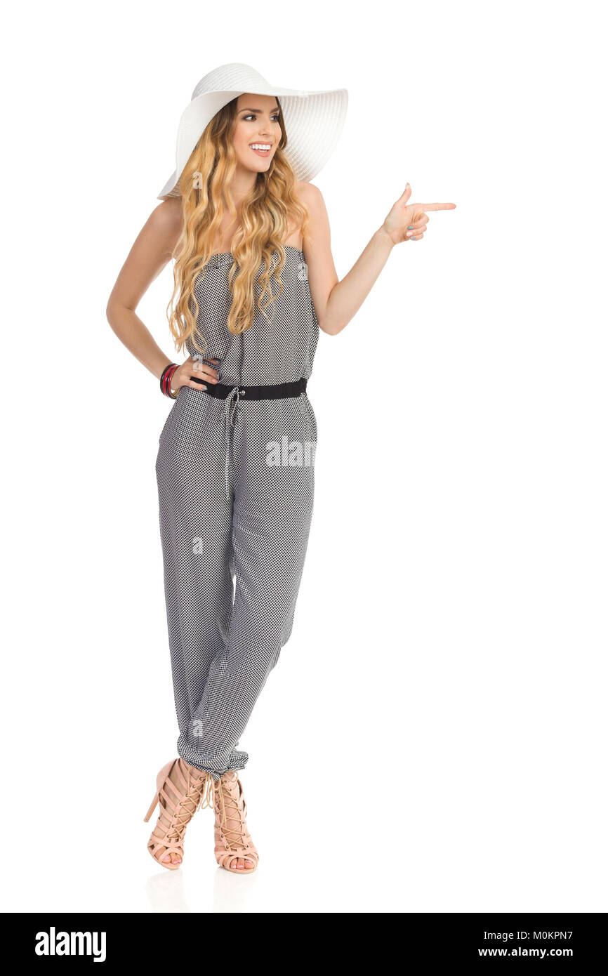 Beautiful young woman in sun hat, jumpsuit and high heels is standing