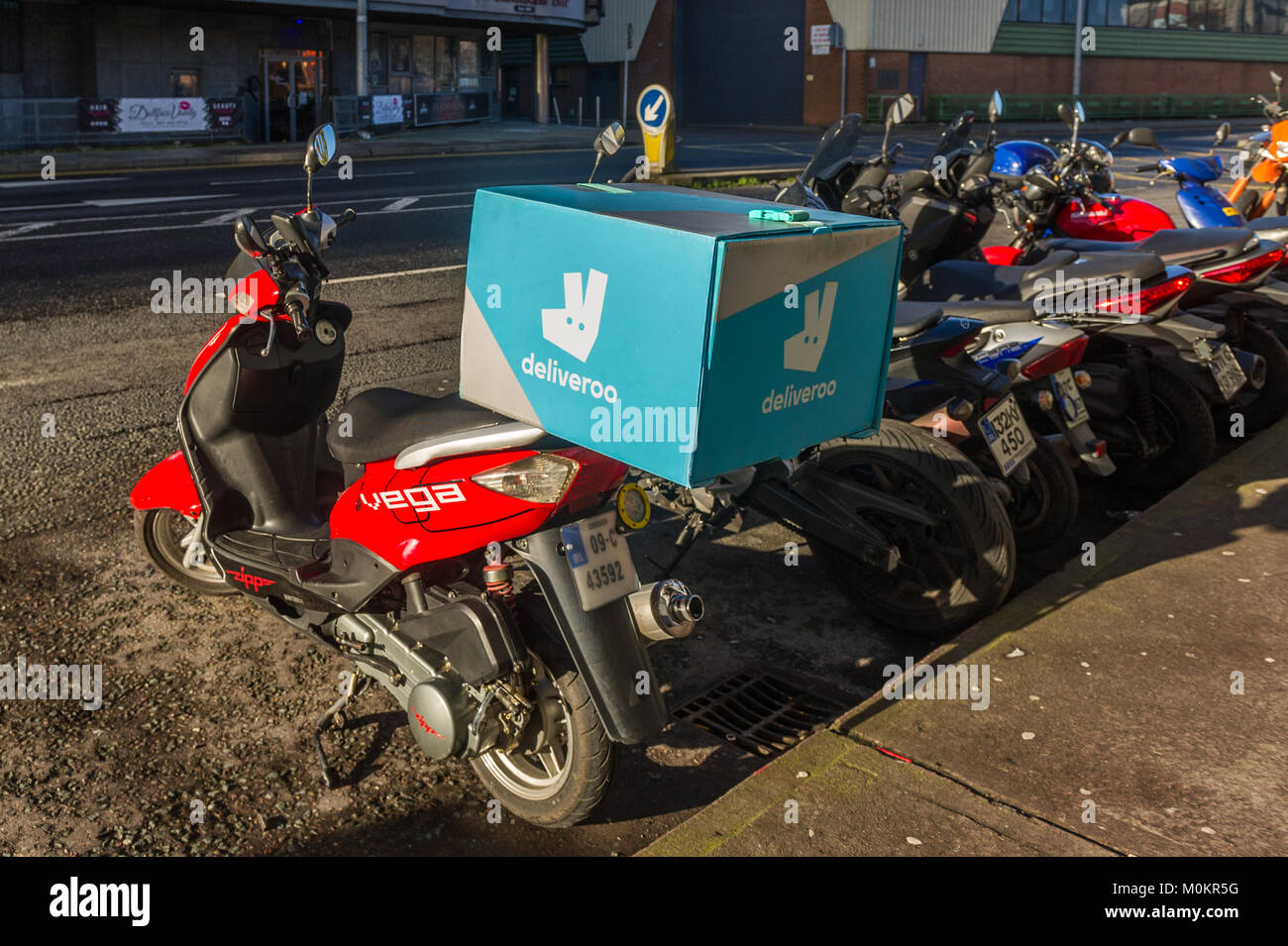 Deliveroo food box on the back of a parked motor scooter on the side of the road in Cork, Ireland. Stock Photo