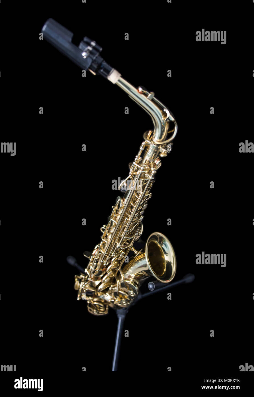 Full view of a golden saxophone standing isolated in black Stock Photo