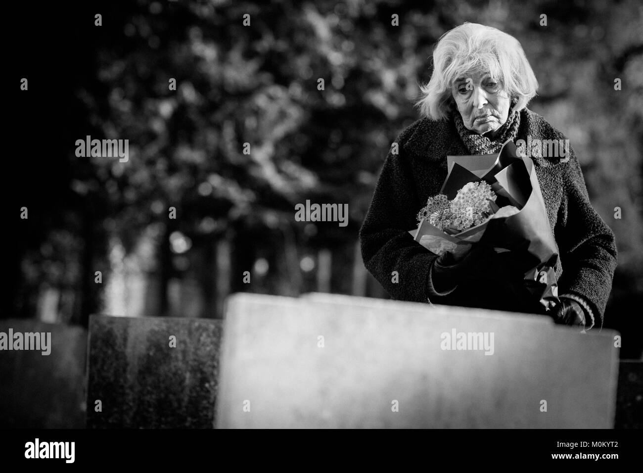 Sad Senior Woman With Flowers Standing By Grave Stock Photo