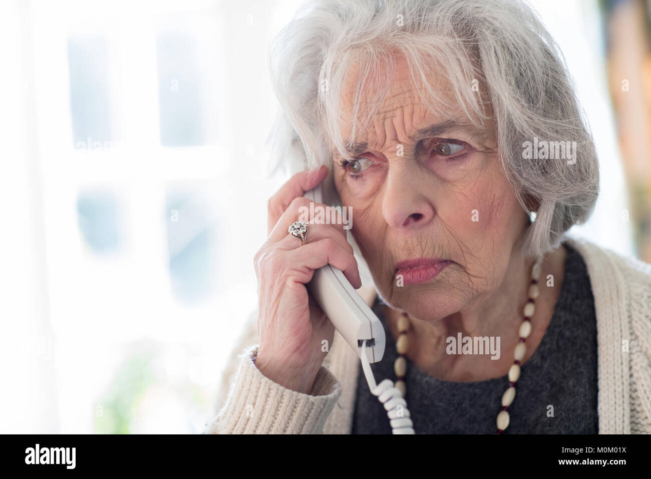 Worried Senior Woman Answering Telephone At Home Stock Photo