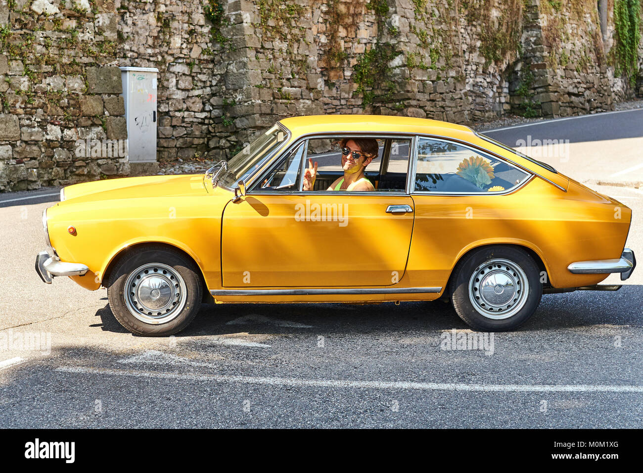 Young man driving yellow vintage Fiat 850 Sport Coupe released circa 1970 in Italy. Stock Photo
