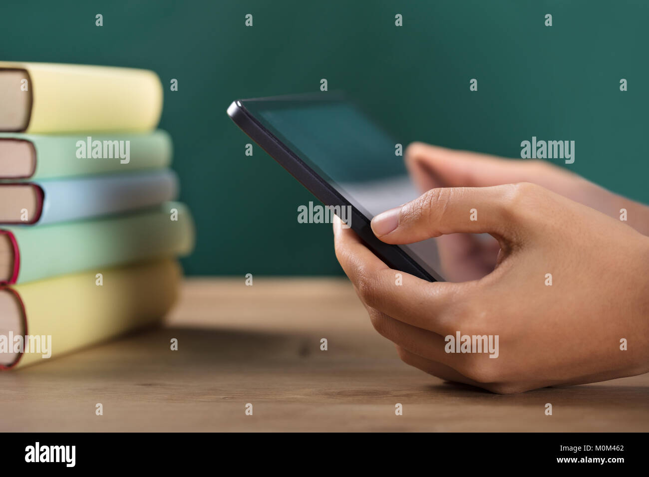 Close-up Of A Student's Hand Using Digital Tablet With Stacked Books On Desk Stock Photo
