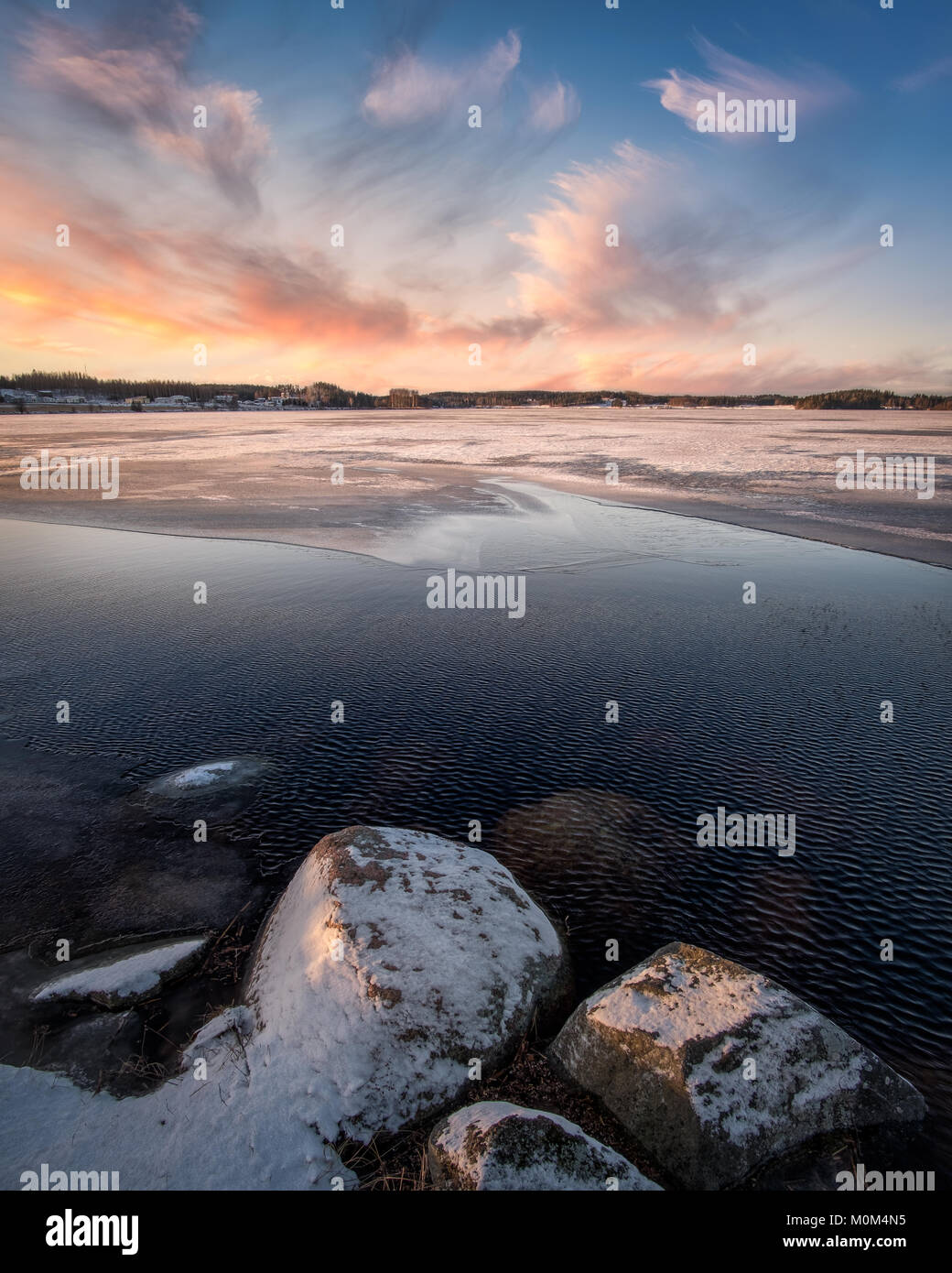 Scenic landscape with sunset and freezing lake at winter evening in FInland Stock Photo
