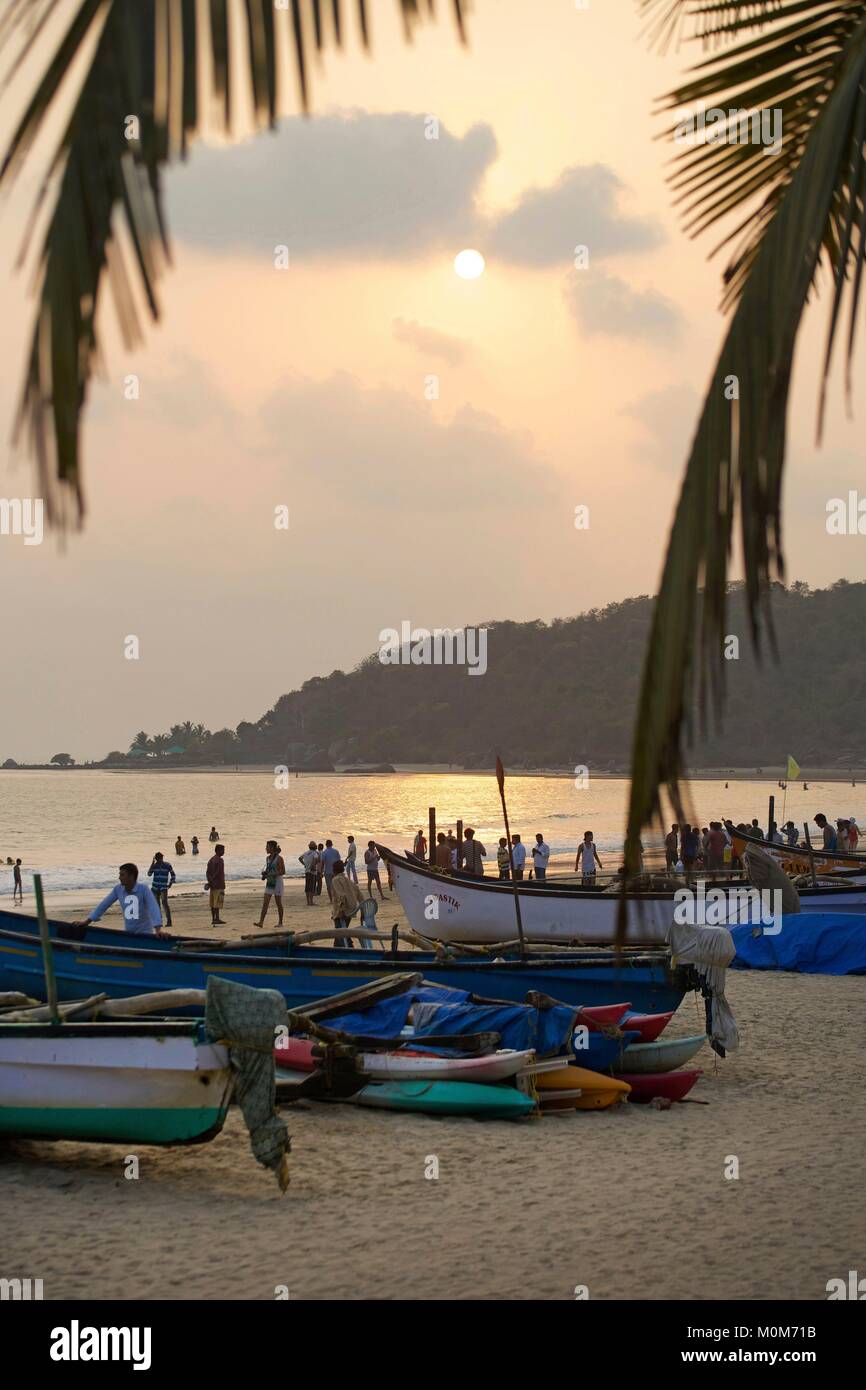 India,Goa,Palolem,tourists in the golden sand beach lined with coconut trees,in front of fishermen boats,at sunset Stock Photo