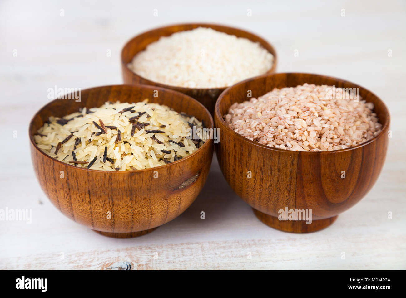 Three bowls with different varieties of rice on a wooden background ...