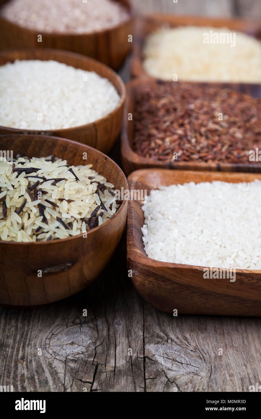 Six bowls with different varieties of rice on a wooden background