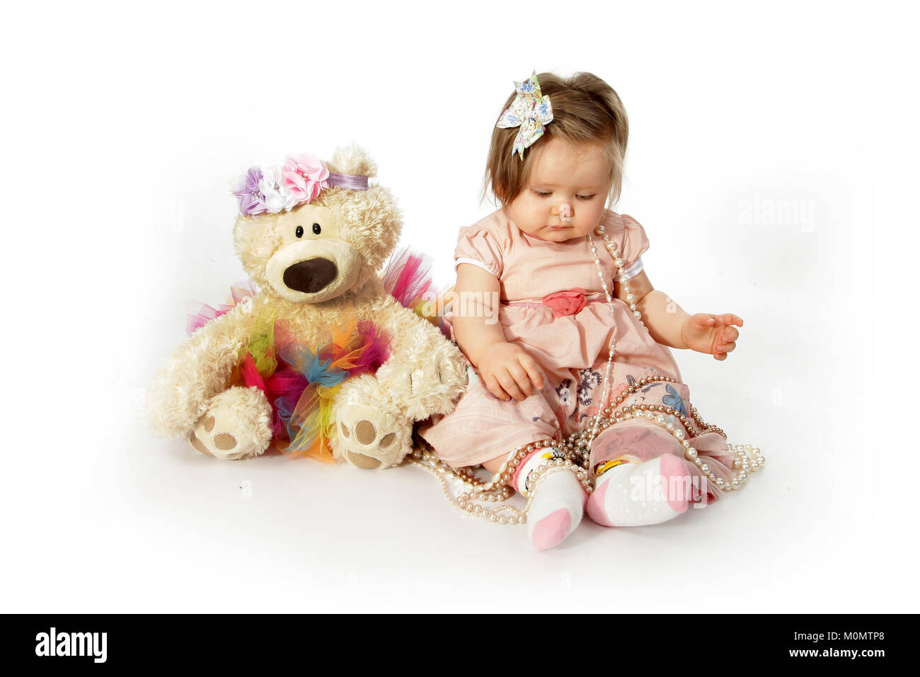 1 year old beautiful girl in pretty dress, playing with teddy, personal and social skills Stock Photo
