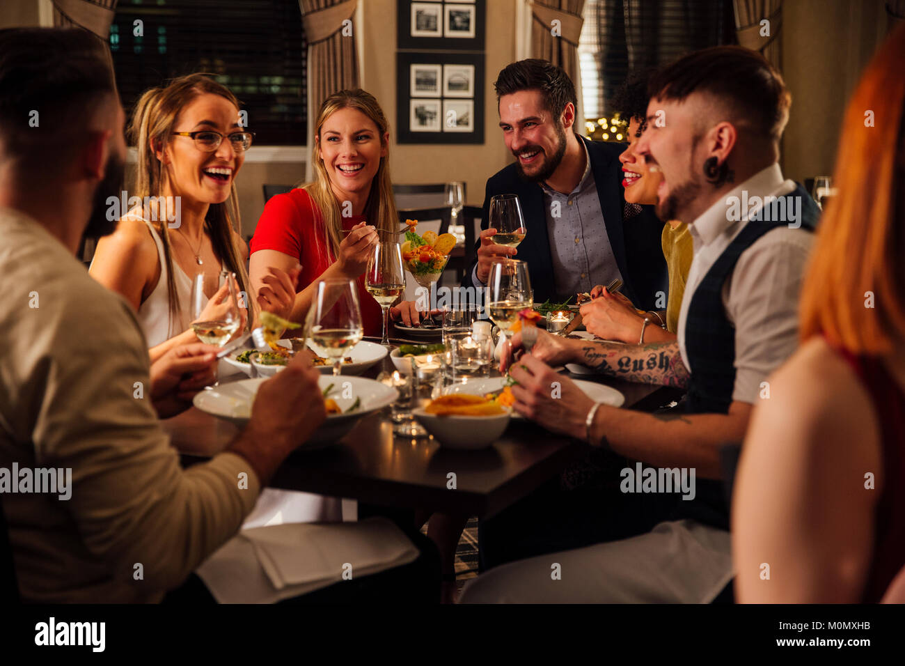 Group of friends are enjoying a meal together. They are talking and laughing while eating their starters and drinking champagne. Stock Photo