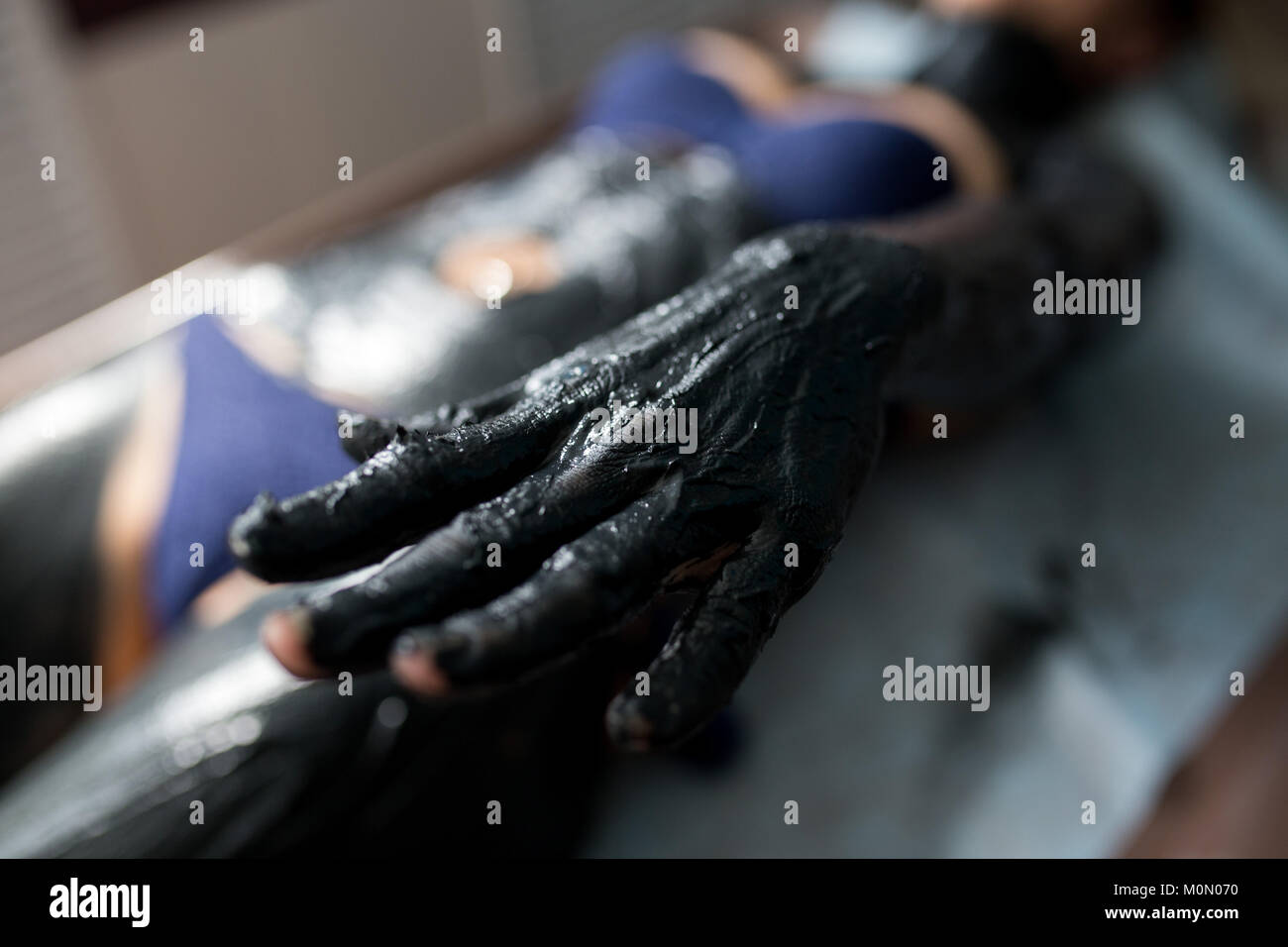 Young woman getting spa treatment in salon. Beautiful girl having clay body mask apply. Mud therapy. Close up of hand Stock Photo