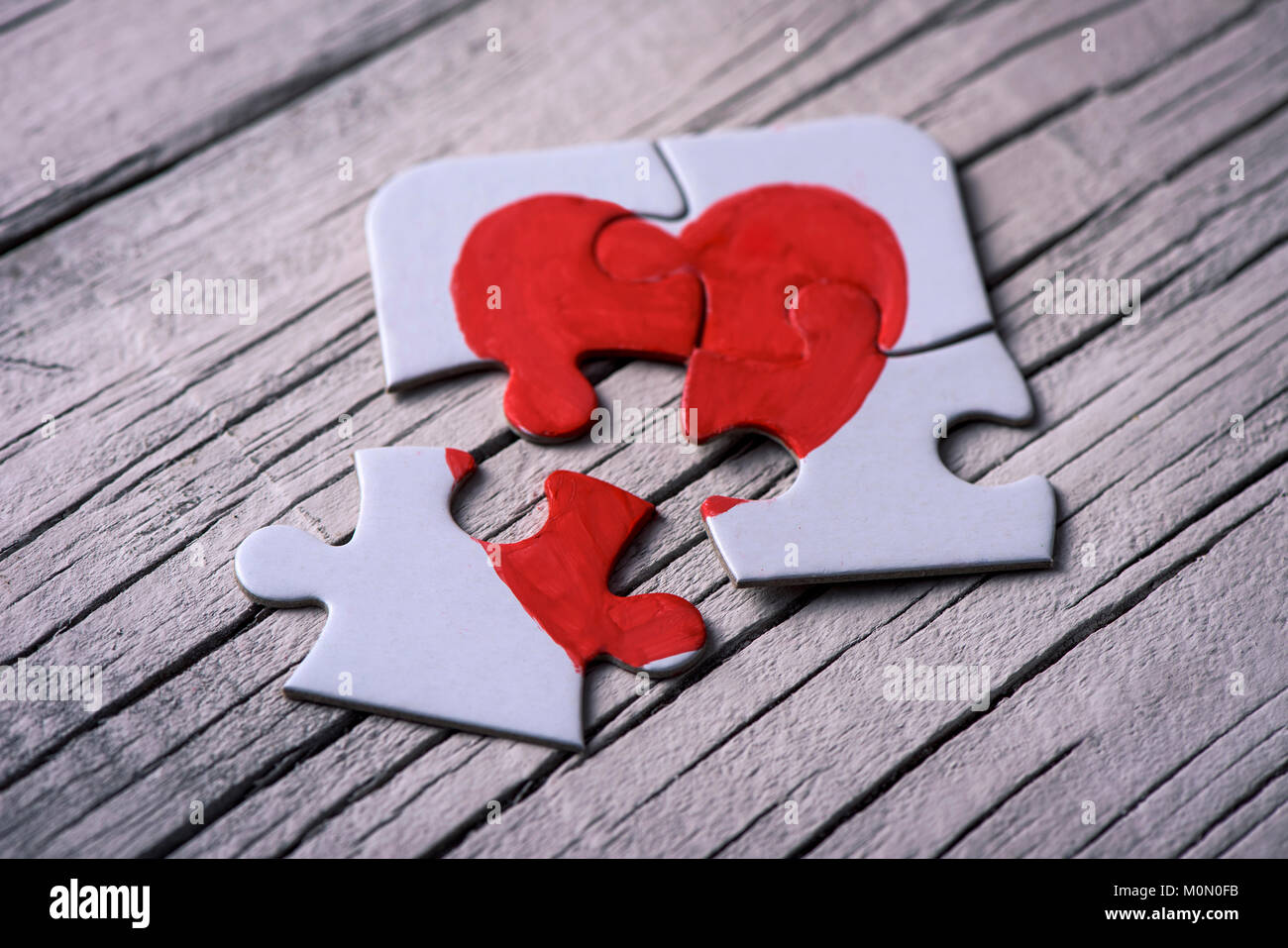 closeup of some separated pieces of a puzzle which together form a heart on a white rustic wooden surface, depicting the idea of rupture or cooperatio Stock Photo
