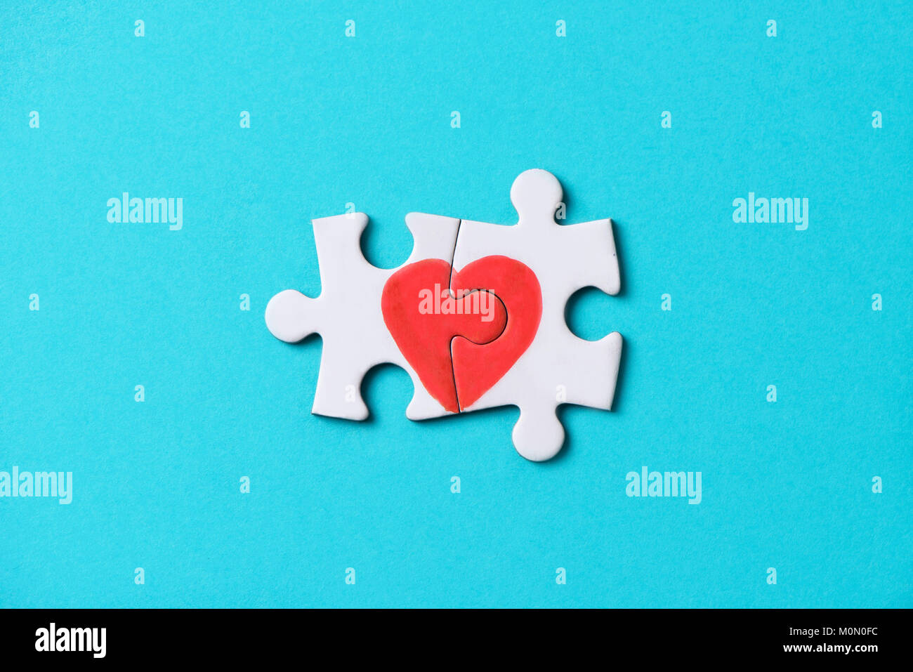 closeup of two pieces of a puzzle forming a heart, depicting the idea that love is a matter of two, on a blue background, with some blank space around Stock Photo