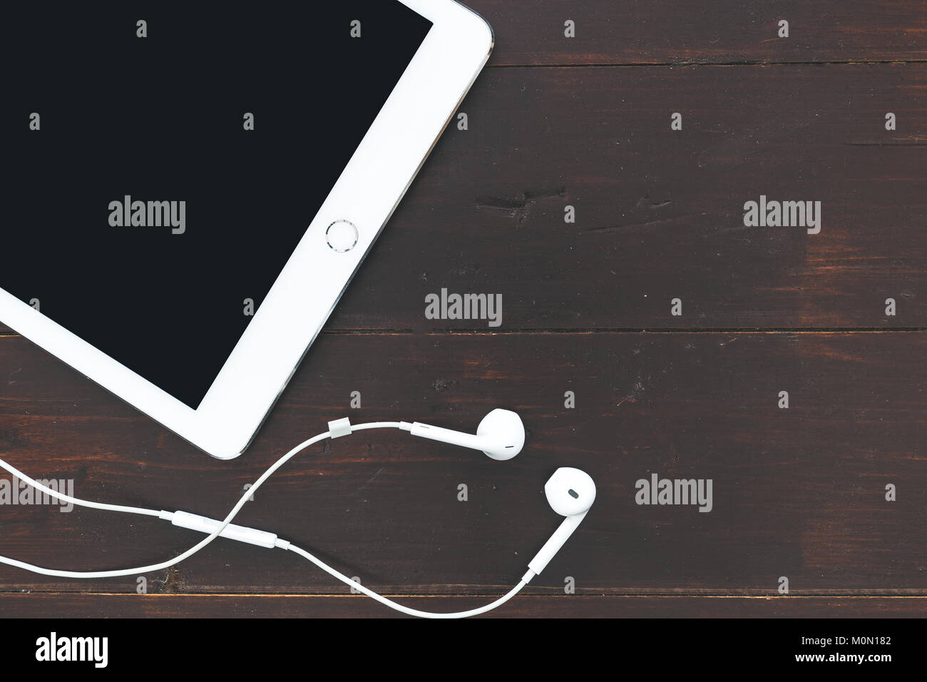 White tablet computer music earphones overhead on dark brown table background Stock Photo