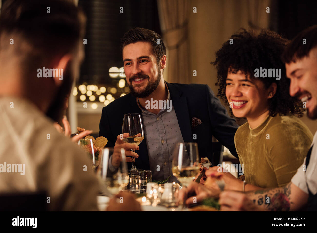 Group of friends are enjoying a meal in a restaurant. They are are talking and laughing while eating and drinking wine. Stock Photo
