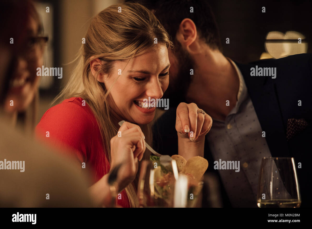 Couple are being romantic while having a meal in a restaurant. The man is kissing the woman on on the cheek and she is giggling. Stock Photo