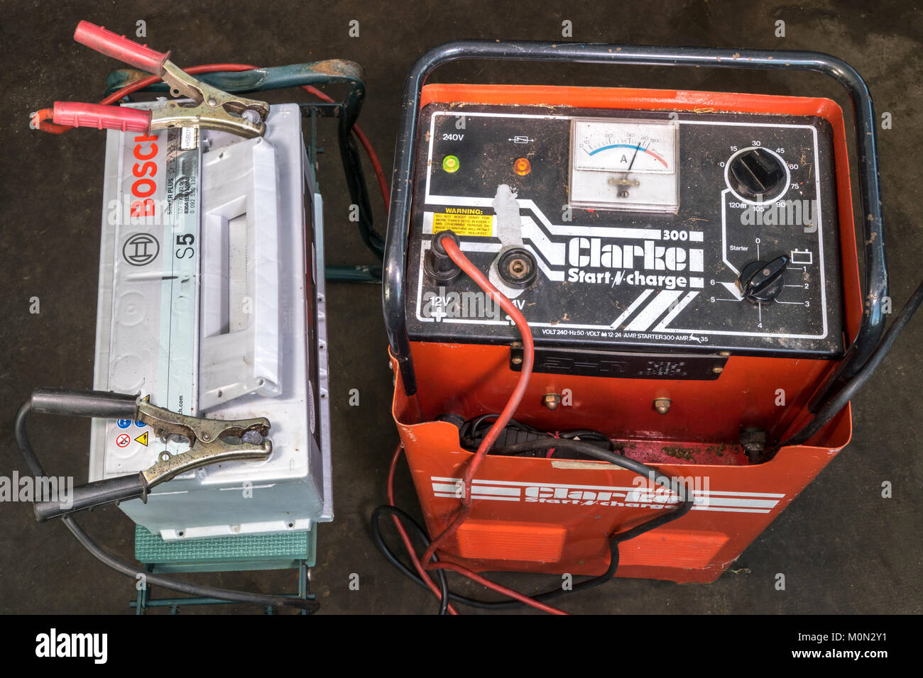 On charge: a flat 12 volt car battery connected to, and receiving a charge from, an industrial, heavy duty, Clarke garage charger. England, UK. Stock Photo