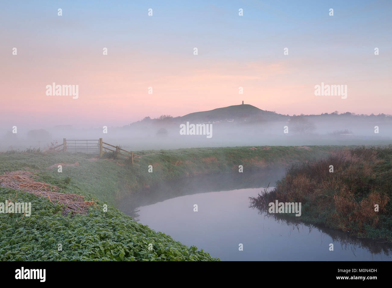 St Michael's Tower and Glastonbury Tor come into view at sunrise as the mist over the River Brue clears. Somerset, England. Stock Photo