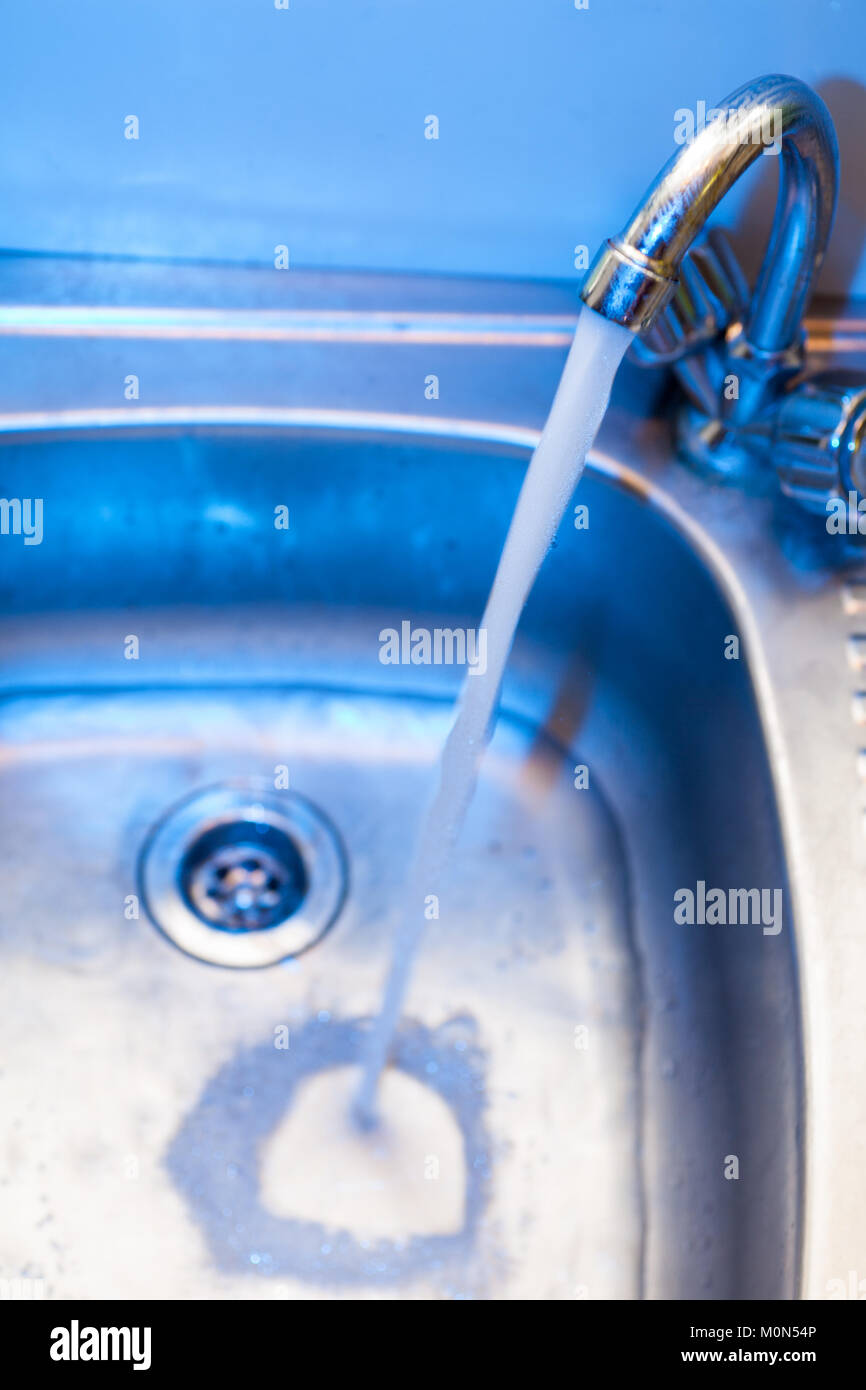 A stream of clean water flows into the stainless steel sink in blue tones. Stainless steel sink