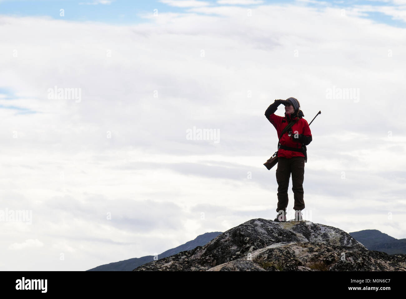 Female tour leader with a rifle stood on high point on look out for Polar Bears to protect tourists visiting Hvalsoy Qaqortoq Kujalleq South Greenland Stock Photo
