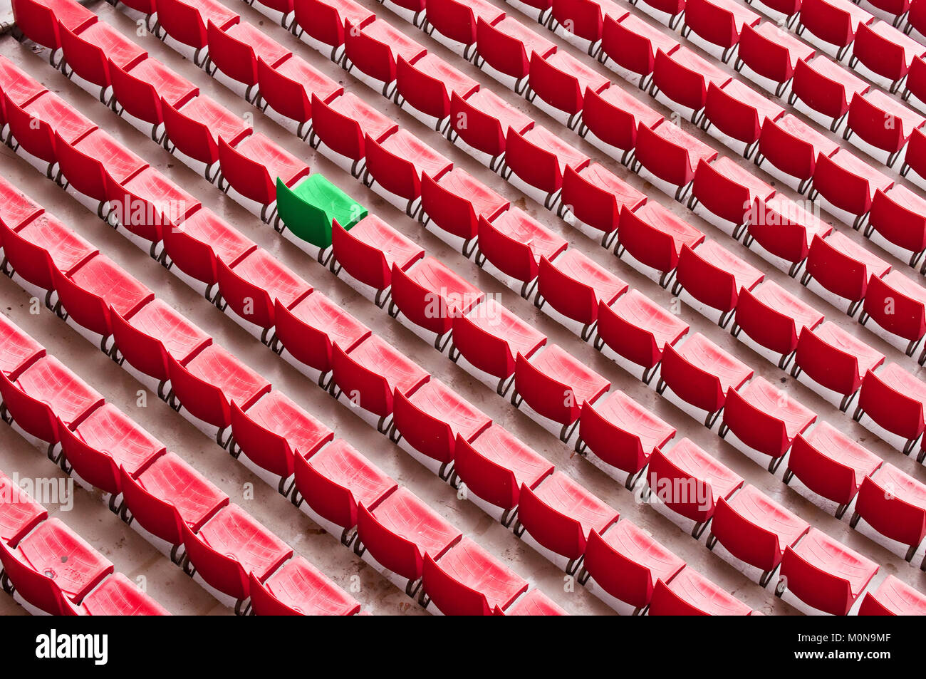 One green seat among red seats in a stadium, standing out of the crowd concept Stock Photo