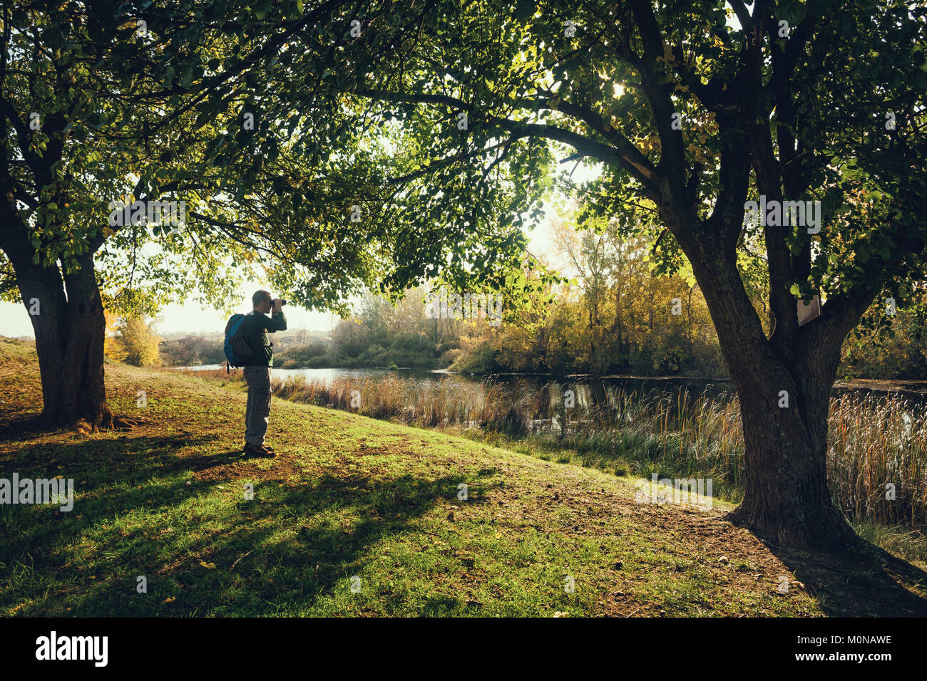 Man is watching birds with binoculars by the river in autumn. Stock Photo